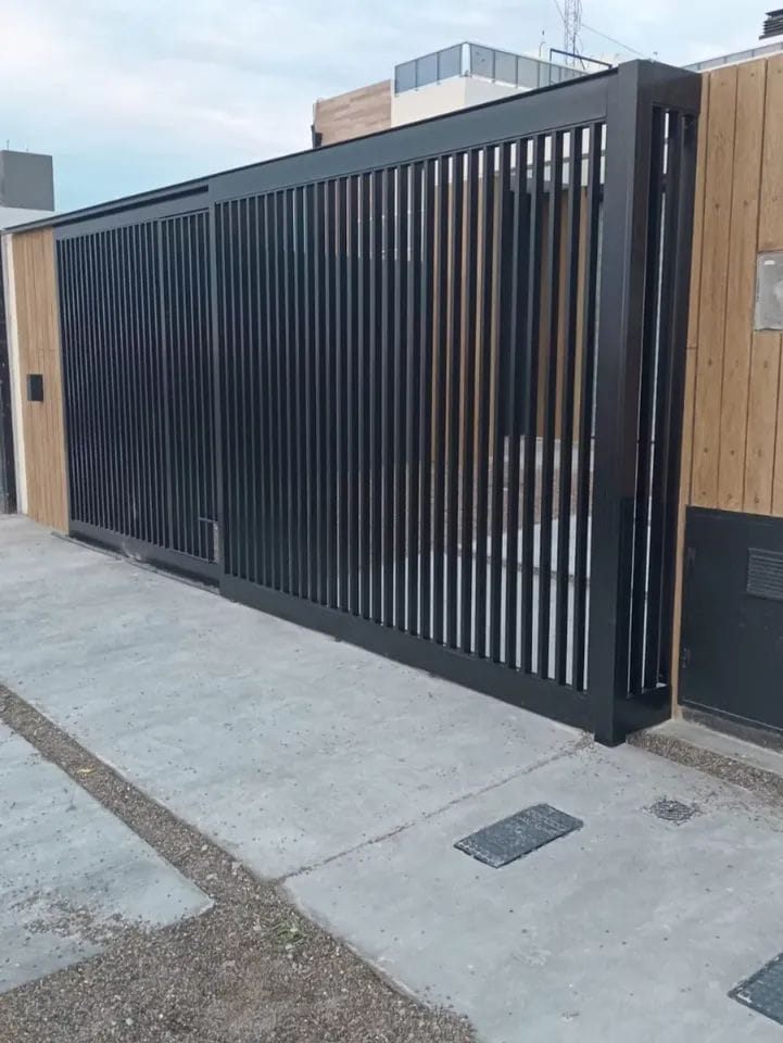 Portón corredizo de aluminio negro con perfiles verticales y puerta peatonal integrada